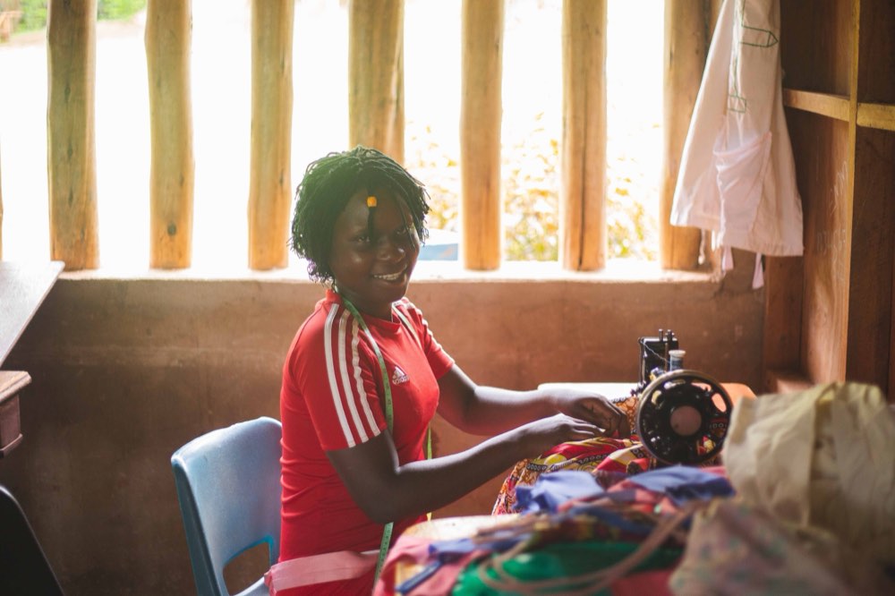 Woman entrepreneur working at her sewing machine, developing her craft (placeholder photo — to be replaced with real YEIB MANCO participant photography before launch)