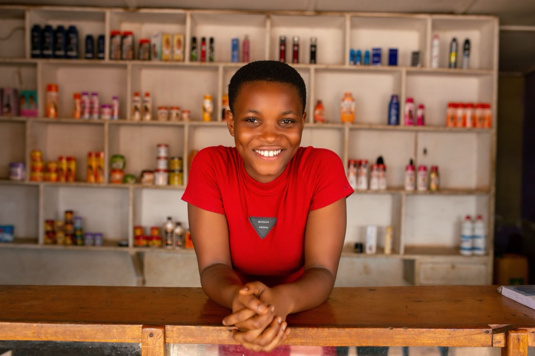Woman entrepreneur smiling behind the counter of her small shop (placeholder photo — to be replaced with real YEIB MANCO participant photography before launch)